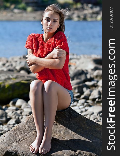 Girl badly frozen sitting on a rock in a red sweater against the rocky shore of the White Sea