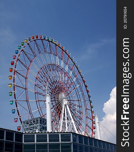 Low angle view of ferris wheel with colorful gondolas and blue sky background.