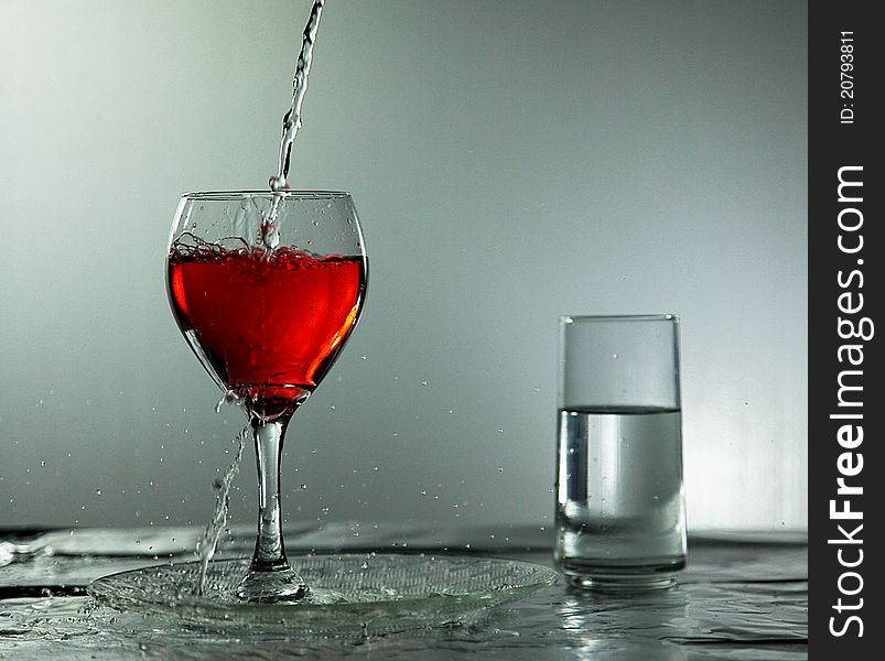 Water being poured into a wineglass with red liquid and spilling over. Water being poured into a wineglass with red liquid and spilling over.