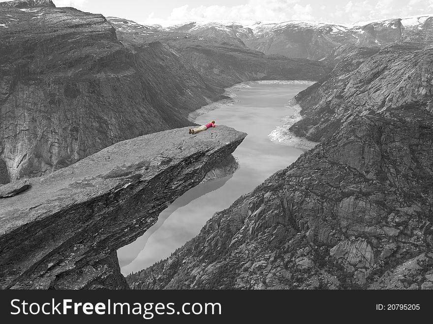 Grayscale photo with girl in color lying on the edge of Troll's Tongue (Trolltunga) in the mountains outside Odda, Norway. In the bacground we can see Folgefonna glacier. Grayscale photo with girl in color lying on the edge of Troll's Tongue (Trolltunga) in the mountains outside Odda, Norway. In the bacground we can see Folgefonna glacier.