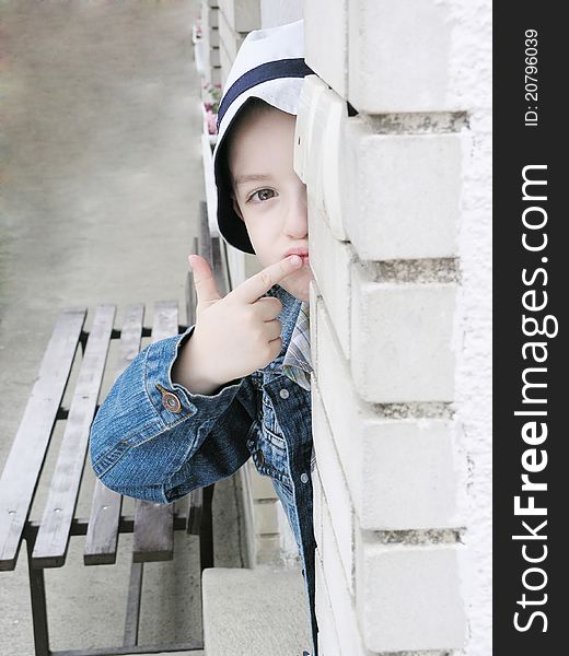 The boy hidden against the wall in a denim jacket with a hat. The boy hidden against the wall in a denim jacket with a hat