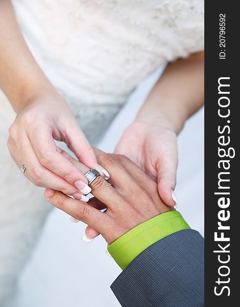 Husband and wife's hands with wedding ring. Bride puts silver band on grooms finger. Brides wedding dress in background. Husband and wife's hands with wedding ring. Bride puts silver band on grooms finger. Brides wedding dress in background.
