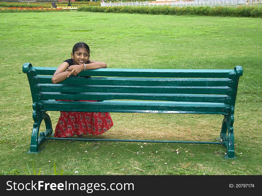 Girl sporting smile sitting back on a green garden bench. Girl sporting smile sitting back on a green garden bench