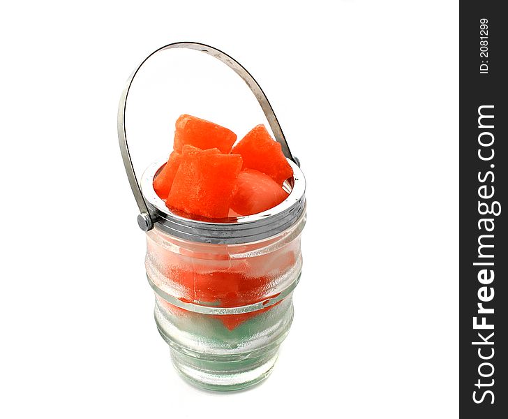 Red ice cubes put in a glass jug with metal handle, view from above on the white background