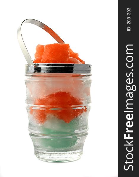 Green, red and white ice cubes put in a glass jug with metal handle on the white background. Green, red and white ice cubes put in a glass jug with metal handle on the white background