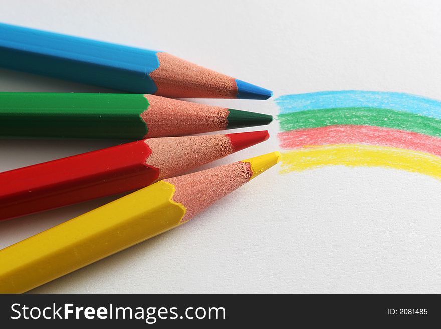 A macro shot of the front end of a group of colored pencils, isolated on white, with the colors of the rainbow drawn on the paper in front. A macro shot of the front end of a group of colored pencils, isolated on white, with the colors of the rainbow drawn on the paper in front