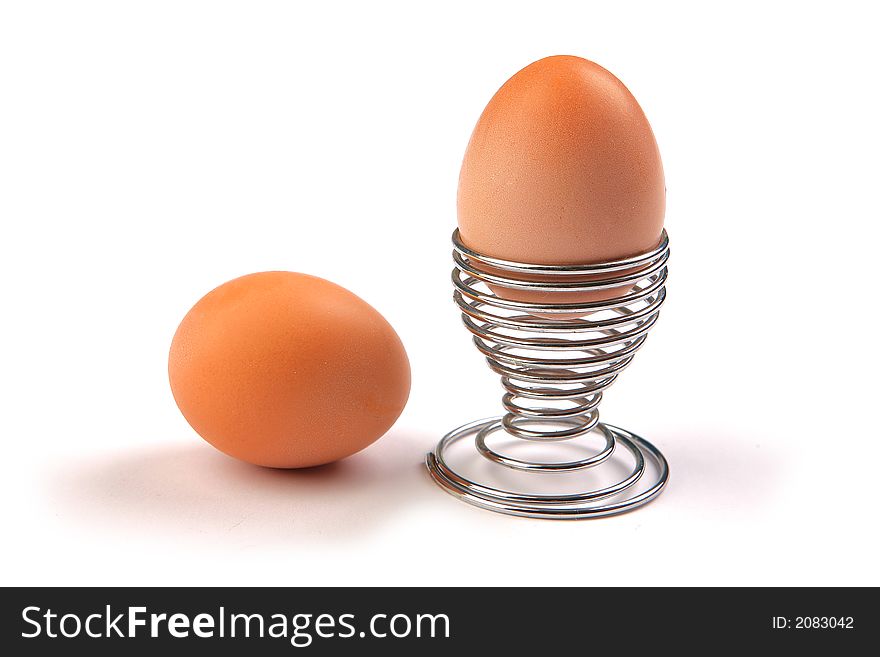 One egg in metal holder and one egg beside that, on white background. One egg in metal holder and one egg beside that, on white background