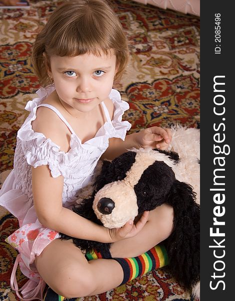 Little girl with toy dog, white dress, sits on floor