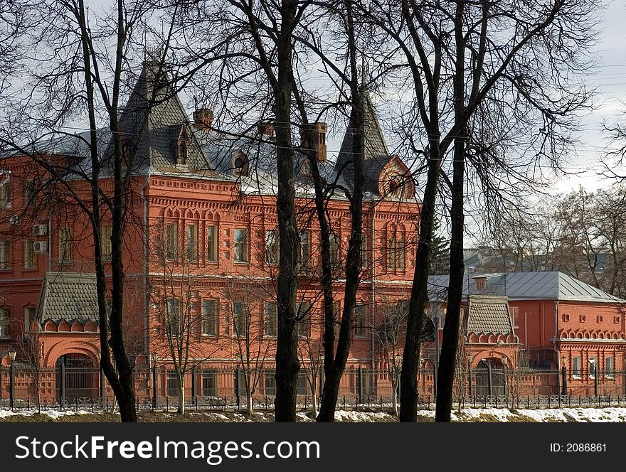 Ancient building from a red brick close up in the late winter with trees in the foreground and the dark blue cloudy sky - on back