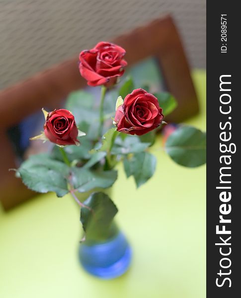 Bouquet of three dark red roses in small blue vase, close shot, photo frame on background. Bouquet of three dark red roses in small blue vase, close shot, photo frame on background