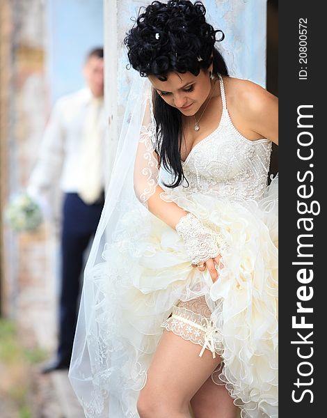 A bride putting on her wedding garter against old grunge place. A bride putting on her wedding garter against old grunge place