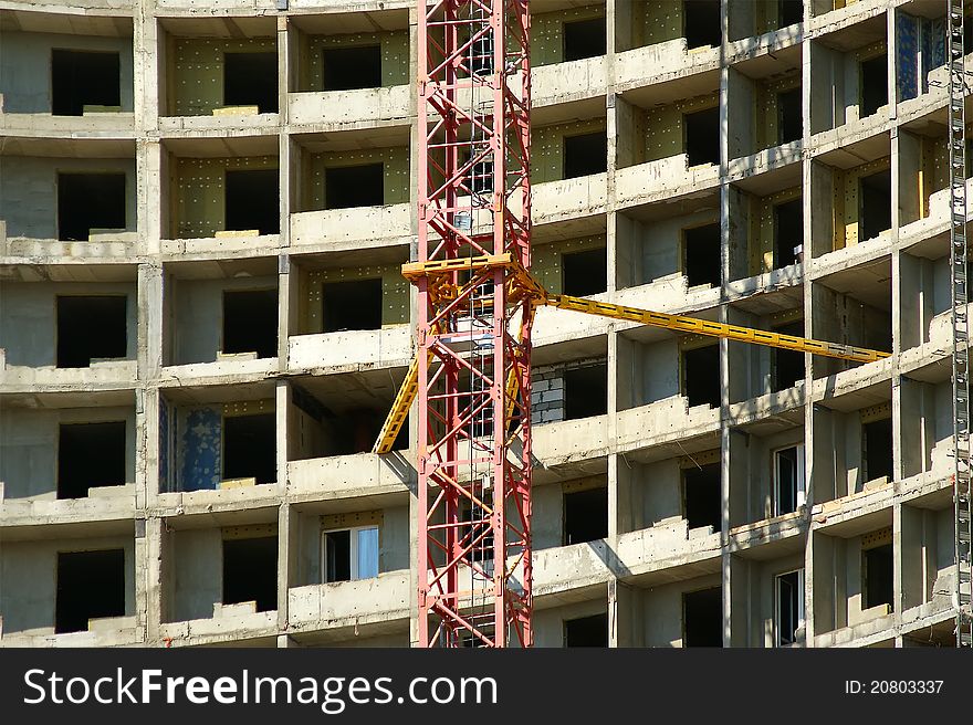 Building crane at the background of a multi-storey building under construction