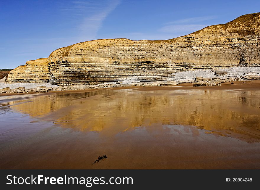 A late winter afternoon at Dunraven Beach, Southerndown, Wales with the cliffs reflecting in the wet sand