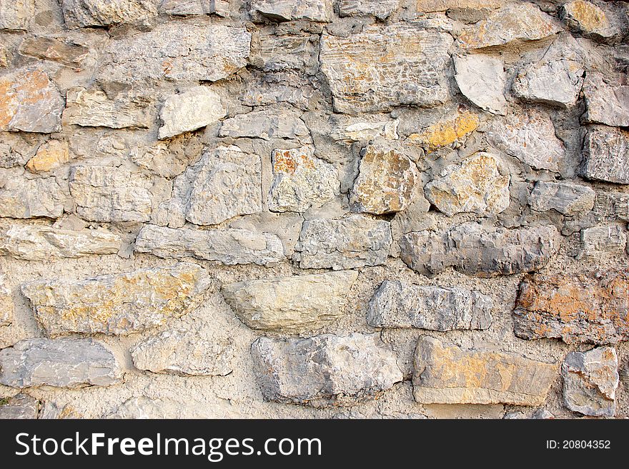 Wall of stones and cement in gray tones with an orange stone in a strong point.