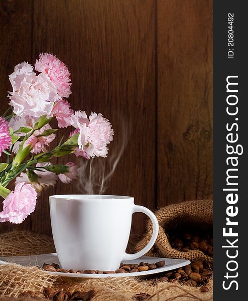 Cup and coffee beans and flowers on dark background.