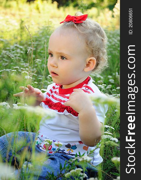 Baby with red bow on the meadow