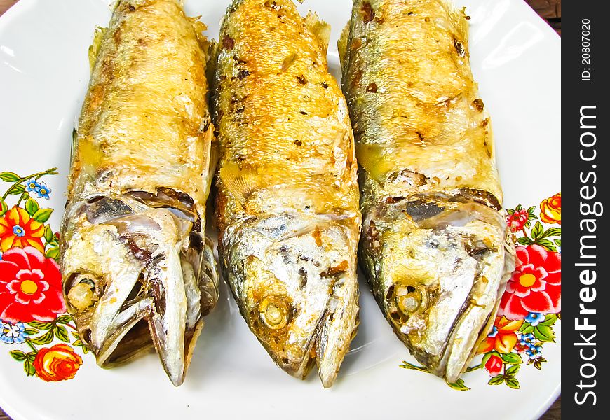 Three fried mackerel on colorful dish