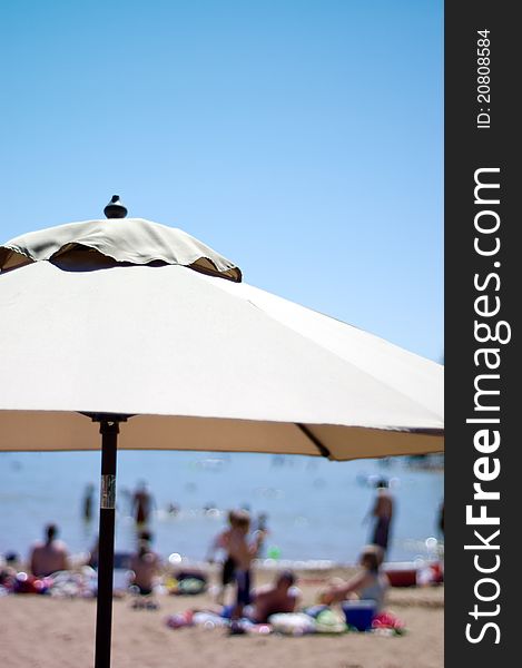 Beach parasol with people in the background at a lake.