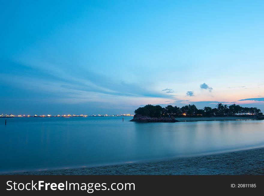 Evening sun setting at dusk over small tropical island with distant ship anchorage in the background, creating a romantic mood. Evening sun setting at dusk over small tropical island with distant ship anchorage in the background, creating a romantic mood.