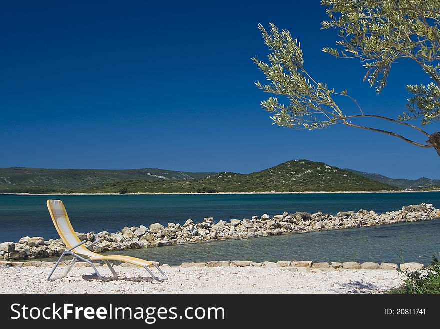 Olive tree and deck chair on the coastline of Turanj with the blue sea and islands. Olive tree and deck chair on the coastline of Turanj with the blue sea and islands