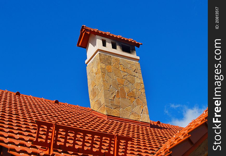 Red ceramic roof. Blue sky background. Flue fased by stone. Snow shield