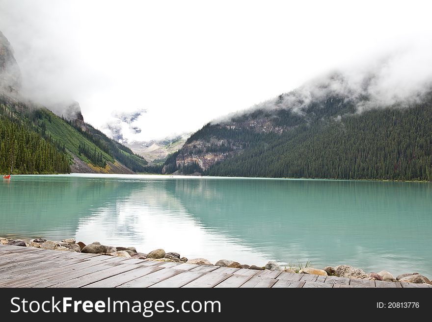 The beautiful turquoise colored Lake Louis against the backdrop of the majestic mountains of the Canadian Rockies partially covered with fog. The beautiful turquoise colored Lake Louis against the backdrop of the majestic mountains of the Canadian Rockies partially covered with fog