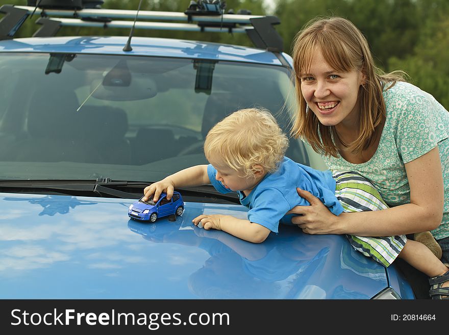 Baby playing car toy on hood with mother