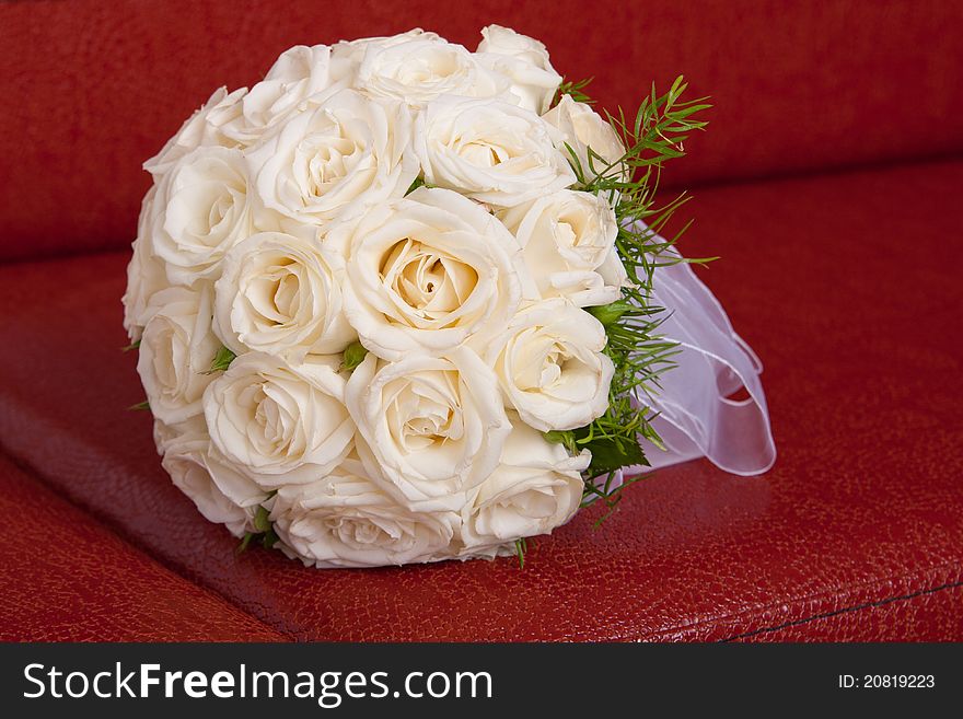 Wedding bridal bouquet of white roses lay on a red couch