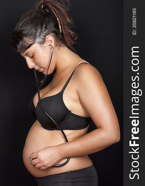 Pregnant woman with stethoscope listening to her belly isolated in black