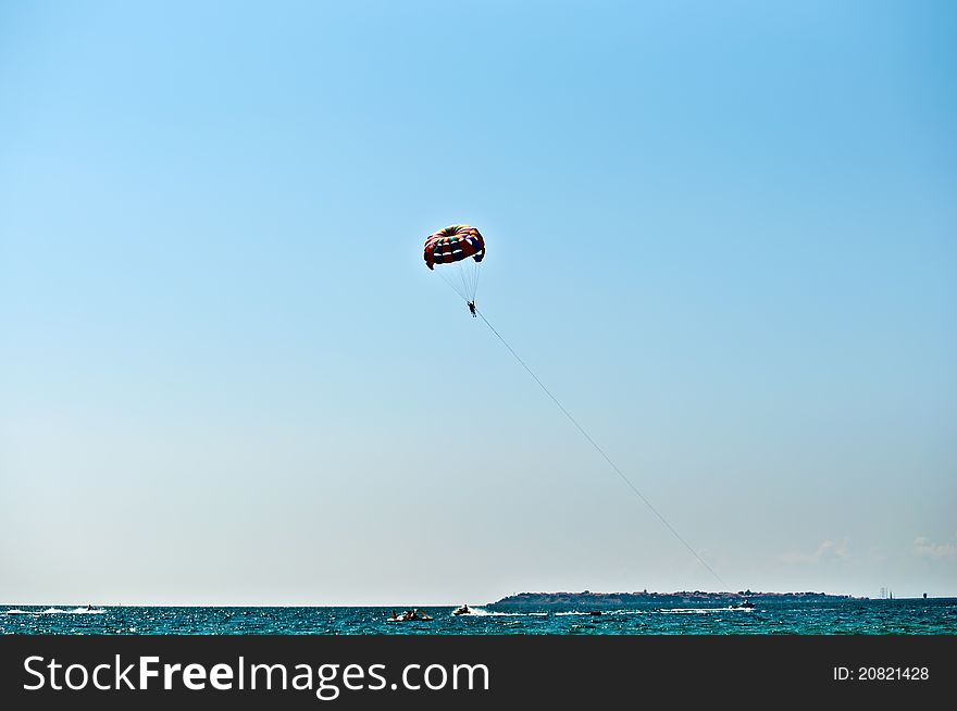 Colorful hang glider in sky over blue sea . Colorful hang glider in sky over blue sea .