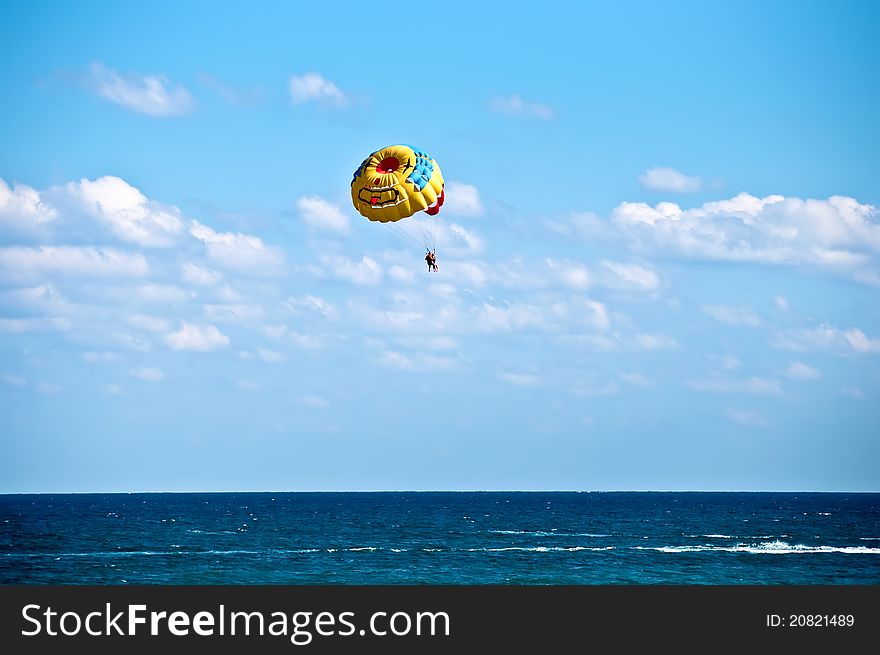 Colorful hang glider in sky over blue sea . Colorful hang glider in sky over blue sea .