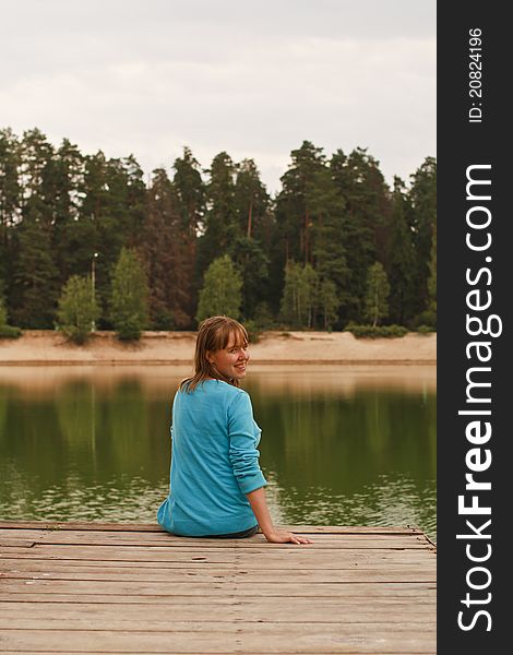 Young woman smiling sitting on jetty on automn lake. Young woman smiling sitting on jetty on automn lake