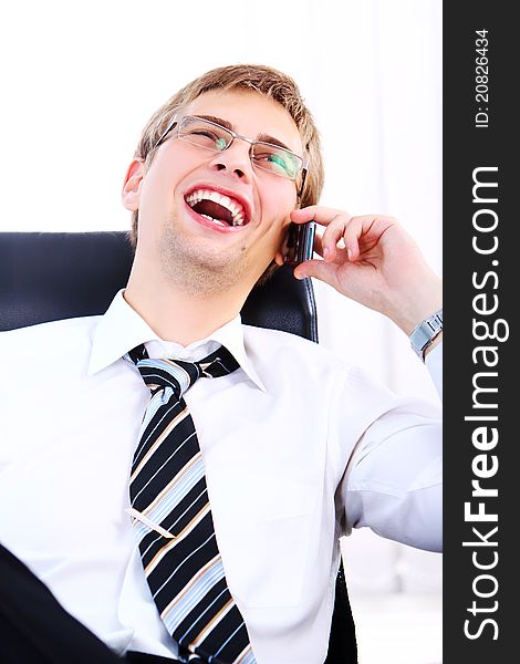 Young and successful businessman with smile uses cell phone in his office. Young and successful businessman with smile uses cell phone in his office
