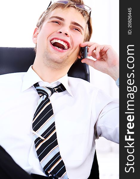 Young and successful businessman with smile uses cell phone in his office. Young and successful businessman with smile uses cell phone in his office