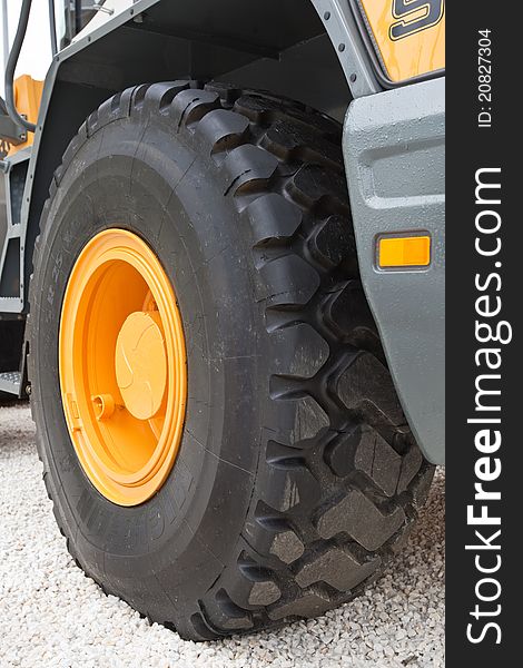 Black wheel with yellow disk of front loader on white stone road