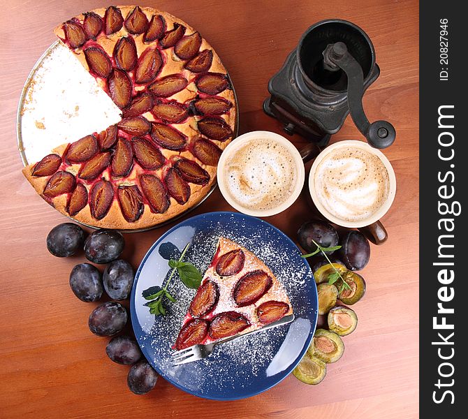 Plum pie, coffee, coffee grinder and plums decorated with mint on a wooden background. Plum pie, coffee, coffee grinder and plums decorated with mint on a wooden background