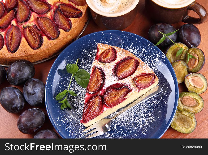 Plum pie, coffee and plums decorated with mint on a wooden background