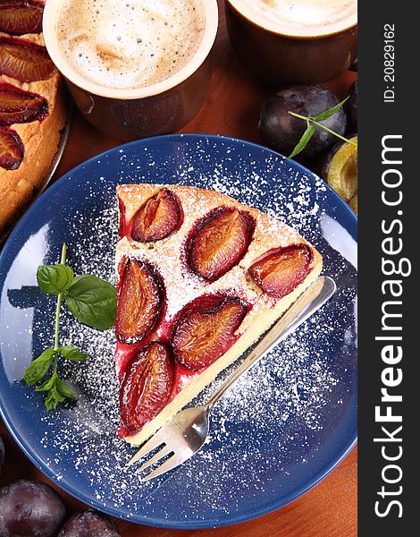 Plum pie, coffee and plums decorated with mint on a wooden background