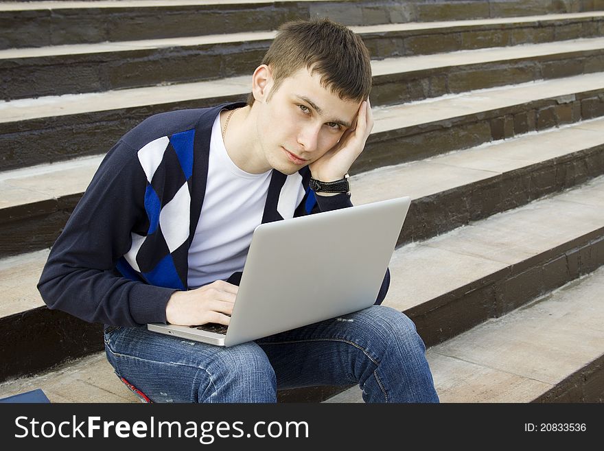 Close-up of a young attractive student on campus sits on a ladder with a laptop. Suffers from headaches. Close-up of a young attractive student on campus sits on a ladder with a laptop. Suffers from headaches
