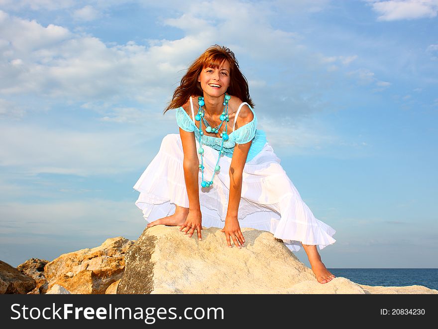 Smiling beautiful woman on a rock looking at the camera on cloudy sky and sea (ocean) background. Smiling beautiful woman on a rock looking at the camera on cloudy sky and sea (ocean) background