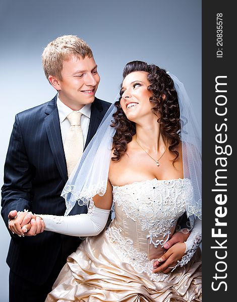 Studio portrait of young elegant enamored just married bride and handsom groom looking to each other and embracing on gray background. Studio portrait of young elegant enamored just married bride and handsom groom looking to each other and embracing on gray background