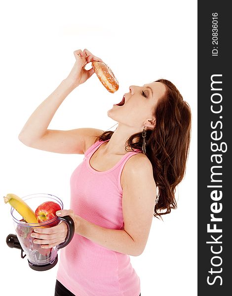 A woman making a smoothie of fruit but taking a bite of a doughnut. A woman making a smoothie of fruit but taking a bite of a doughnut.