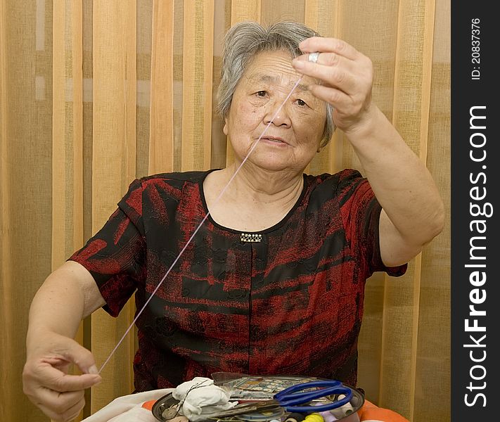 A grandma is sewing at home. A grandma is sewing at home