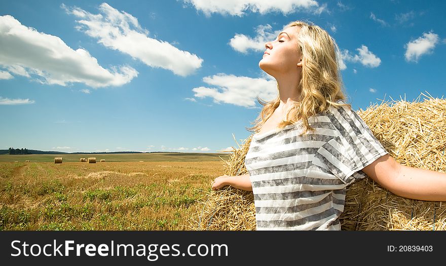 Girl at a stack of straw against a field and the sky