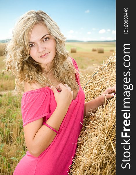 Girl at a stack of straw against a field and the sky