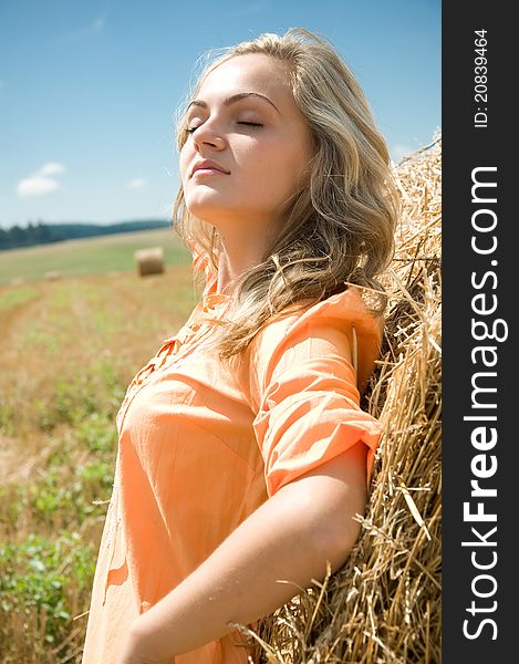 Girl at a stack of straw against a field and the sky
