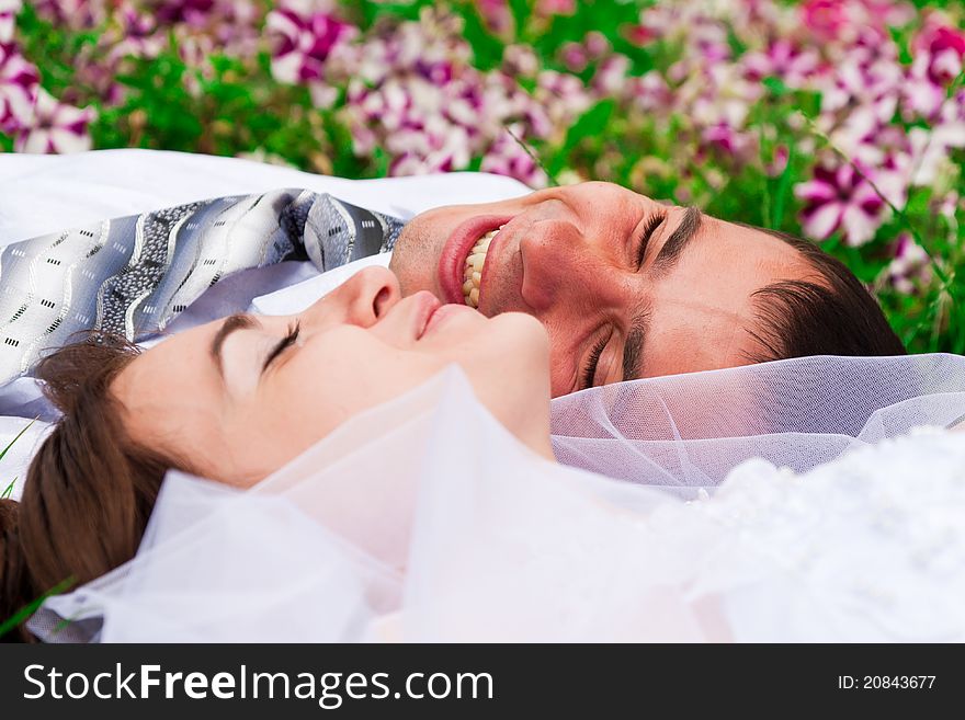 Happy smiling bride and groom  lying on a green grass laughing. Happy smiling bride and groom  lying on a green grass laughing