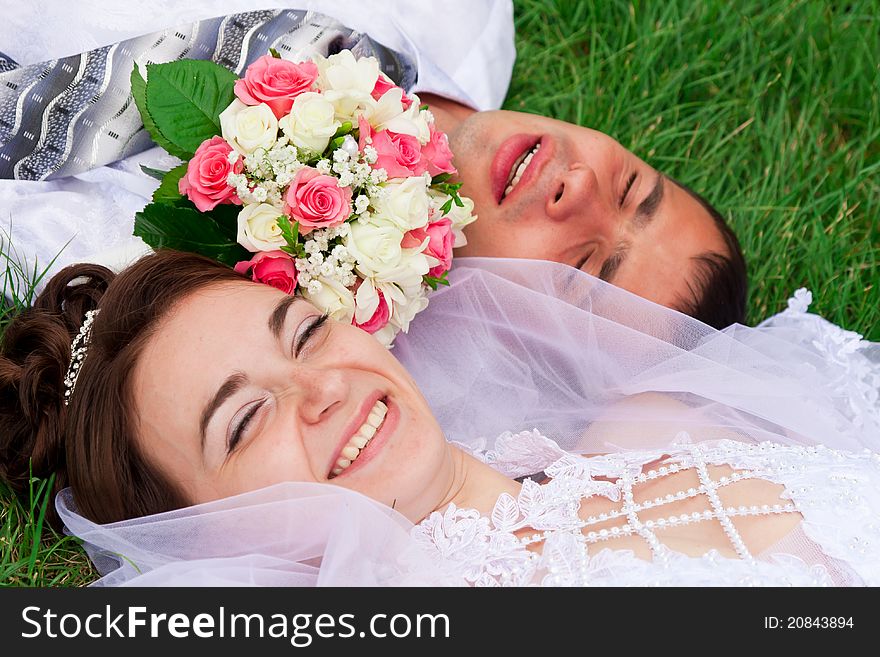 Happy bride and groom lying on a green grass