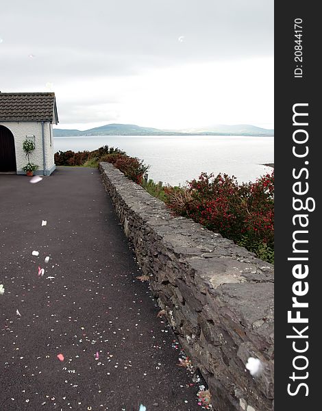 The exterior of an irish church with sea and mountain view and confetti in the air. The exterior of an irish church with sea and mountain view and confetti in the air
