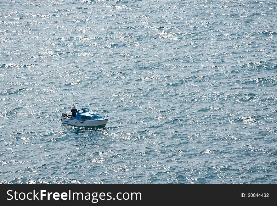 A small boat on the ocean with a fisher and only water around. A small boat on the ocean with a fisher and only water around.